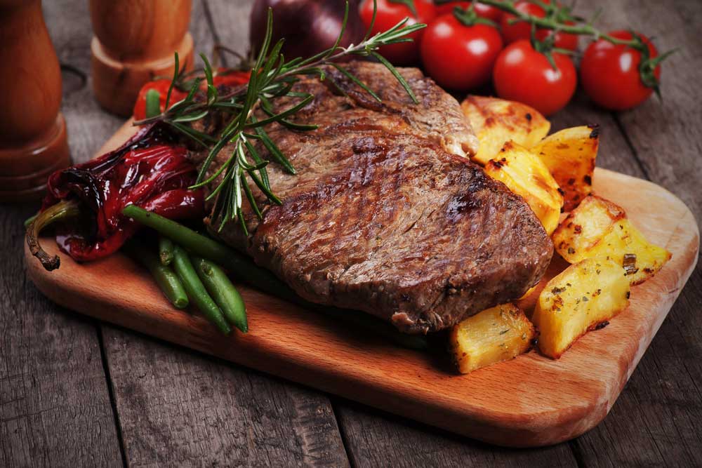 Steak and potatoes on cutting board surrounded by vegetable