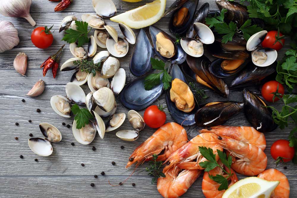 Variety of muscles, clams, and shrimp with parsley, tomatoes, garlic, and peppers, on a wooden table.