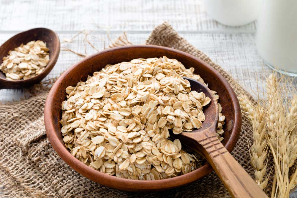 wooden bowl full of oats with a wooden spoon sitting on burlap with stalk of oats next to the bowl