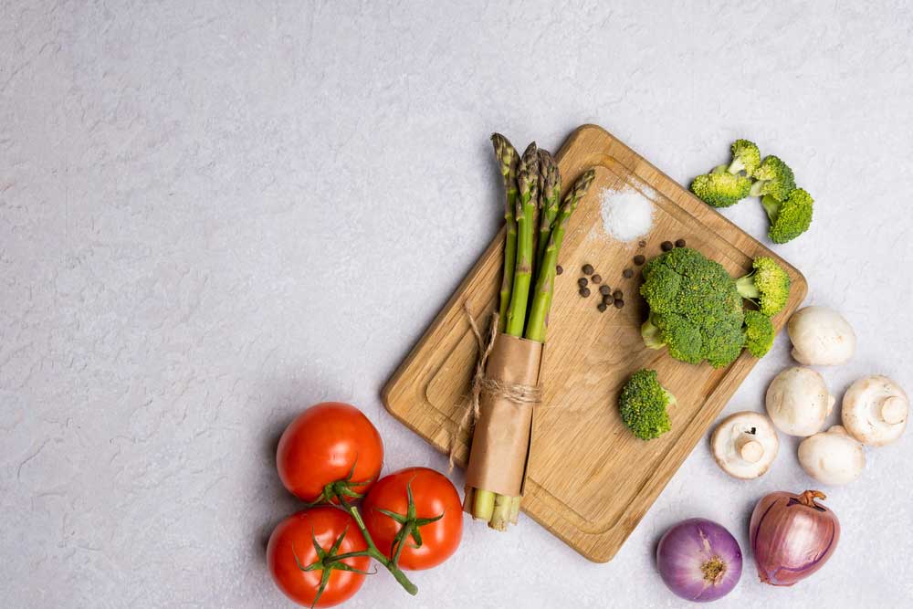 Asparagus and broccoli on a cutting board with spices , tomatoes, onions and mushrooms