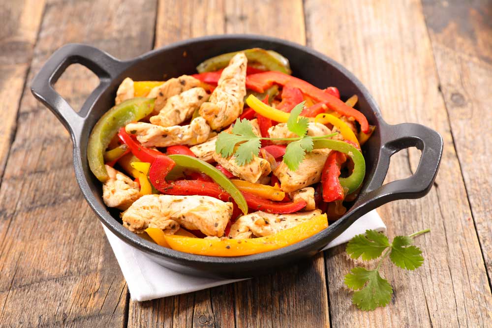 chicken and peppers in an cast iron dish on a wooden table