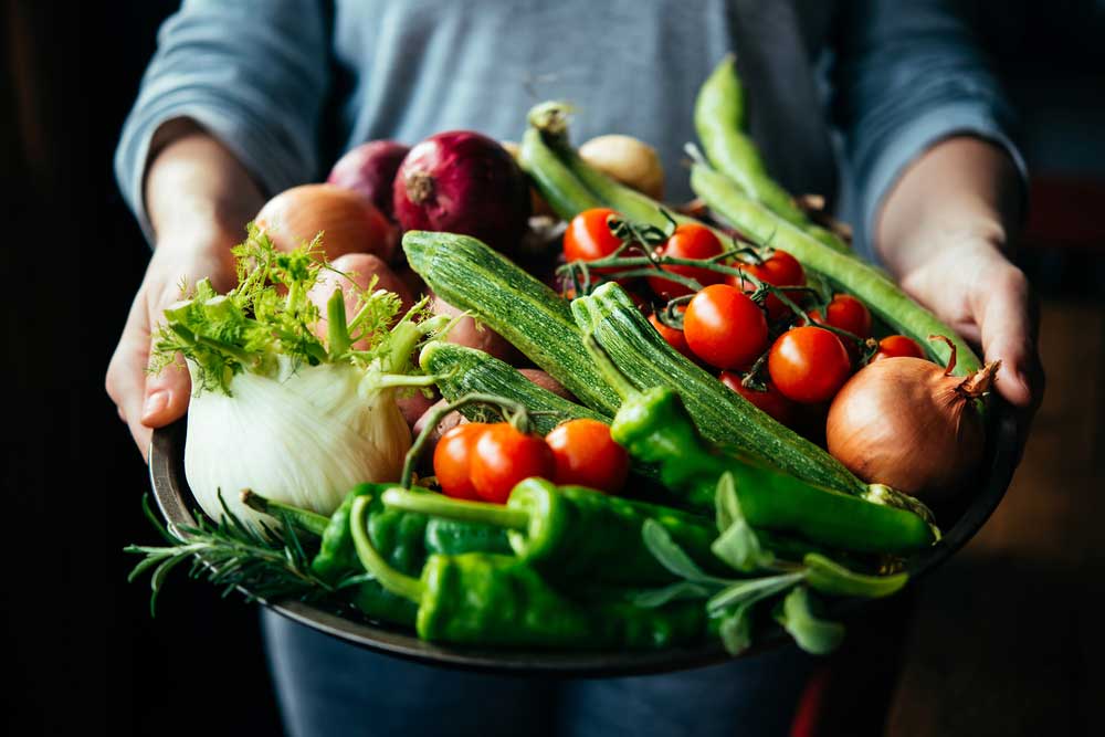 Large bowl of fresh vegetables being offered by human hands