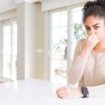 Woman holding nose sitting at kitchen island