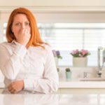 Woman holding her nose standing in the kitchen
