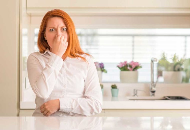 Woman holding her nose standing in the kitchen