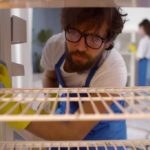 man cleaning the inside of a fridge looking like he wants to be somewhere else