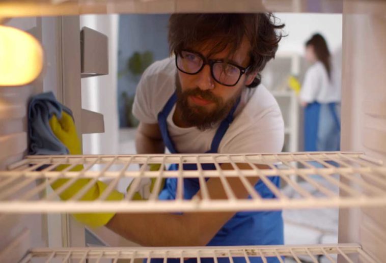 man cleaning the inside of a fridge looking like he wants to be somewhere else