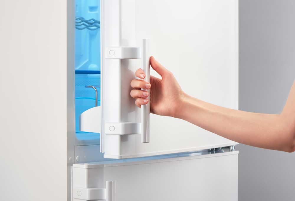 White refrigerator with human arm opening it.