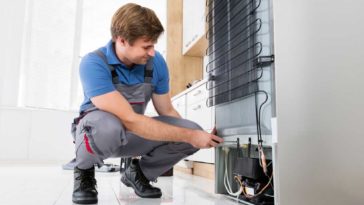 Man kneeling at back of refrigerator to repair it
