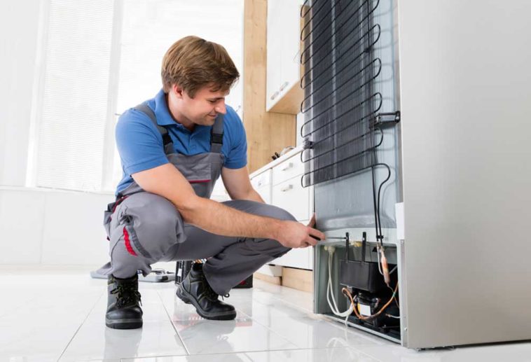 Man kneeling at back of refrigerator to repair it