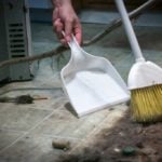 Dirt under a fridge being swept into a dust pan