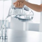 Someone pouring a glass of water from a clear glass pitcher.