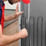 Man unscrewing screw from the back side of a fridge