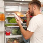 man with freezer open holding his nose while looking at a package of meat