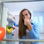 woman looking into open fridge while pinching her nose