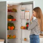 Woman standing in front of open fridge holding her nose