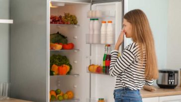 Woman standing in front of open fridge holding her nose
