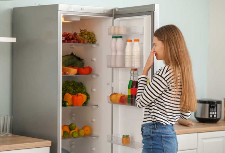 Woman standing in front of open fridge holding her nose