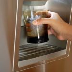 Hand holding glass up to water dispenser on fridge door