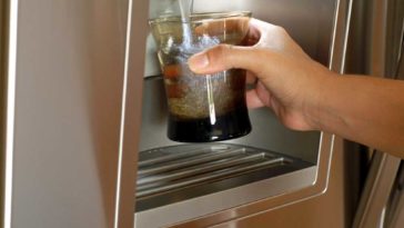 Hand holding glass up to water dispenser on fridge door