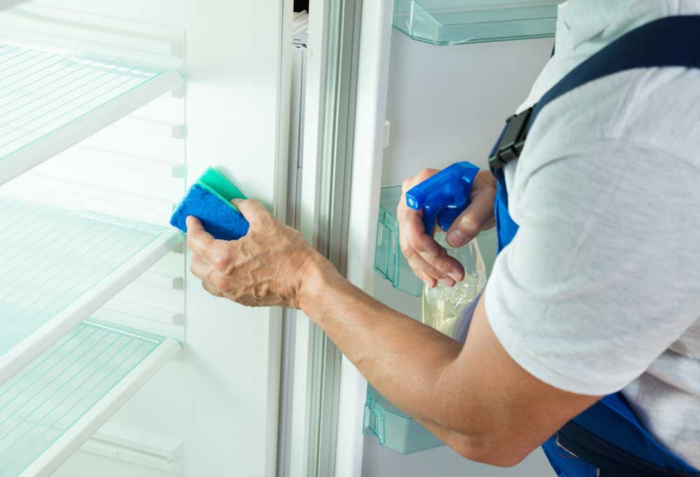 person cleaning the fridge with a blue sponge and spray bottle