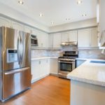 Stainless steel fridge with a dent in the door in a clean kitchen