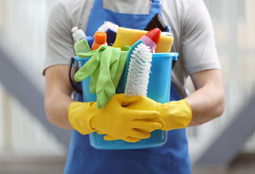 Person holding a bucket of cleaning supplies wearing bright yellow gloves
