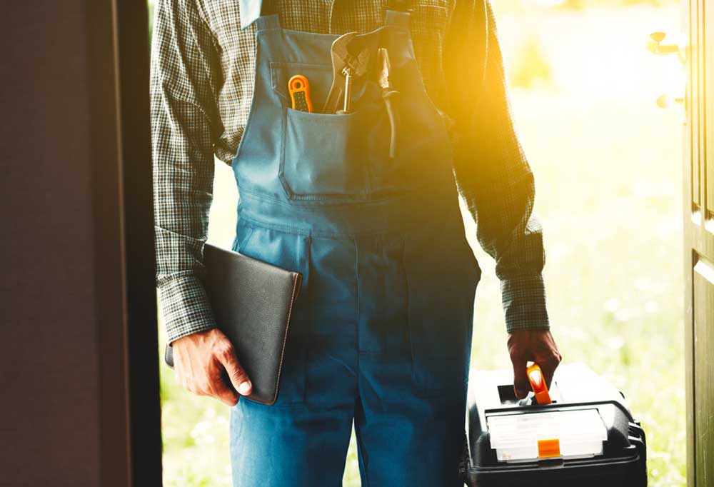 Handyman coming through a door with a notebook and toolbox
