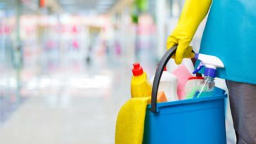 Person with a yellow gloved hand holding a blue bucket full of cleaning supplies