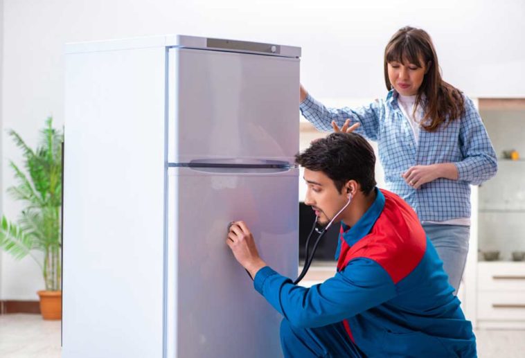 repair man with stethoscope listening to fridge while home owner looks on