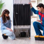 Man and woman kneeling behind broken fridge