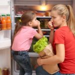 Woman and child kneeling in front of fridge to put away groceries and holding their noses