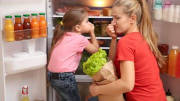 Woman and child kneeling in front of fridge to put away groceries and holding their noses