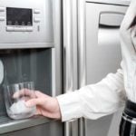 Girl holding glass up to icemaker in door