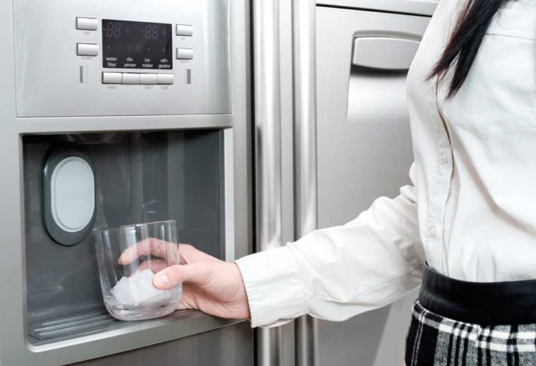 Girl holding glass up to icemaker in door