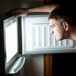 Man standing with freezer door open with light on inside freezer