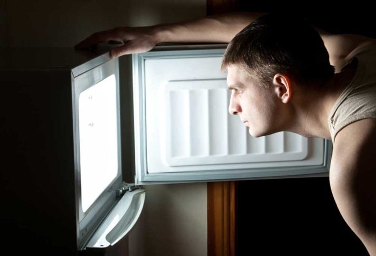 Man standing with freezer door open with light on inside freezer