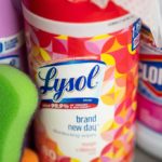 Container of Lysol wipes, can of Lysol spray, bottle of Clorox bleach and a green sponge.