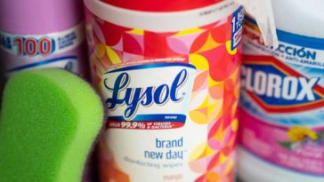 Container of Lysol wipes, can of Lysol spray, bottle of Clorox bleach and a green sponge.