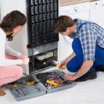 Man and woman kneeling at the back of a fridge with tools