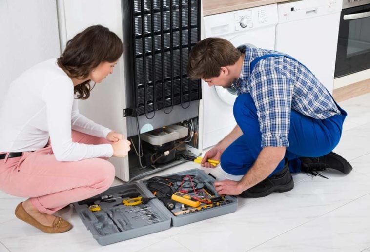 Man and woman kneeling at the back of a fridge with tools