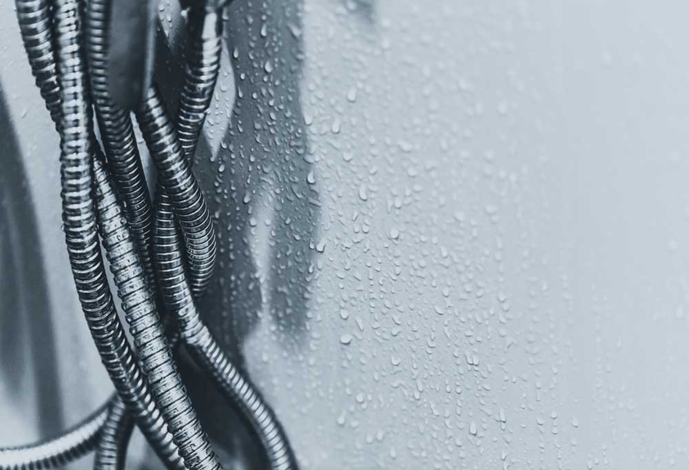 Flexible metal tubing against a white background surrounded by water droplets