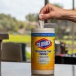 Yellow canister of Clorox wipes on a counter with a hand pulling a wipe out of the top of the container.