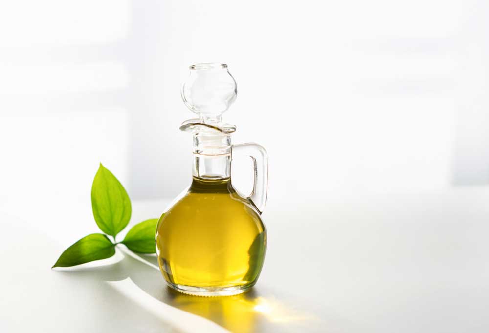 Decanter of olive oil on a white surface with an olive branch
