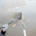close up of ceiling texture being scraped off with a tool on a pole