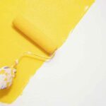 a paint roller painting bright yellow diagonally on a white wall