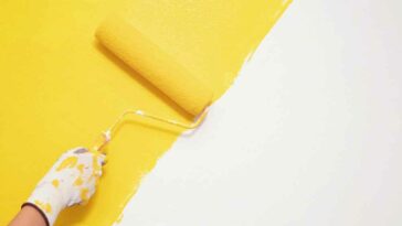 a paint roller painting bright yellow diagonally on a white wall