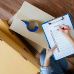 Person checking off checklist of clip board leaning on top of moving boxes