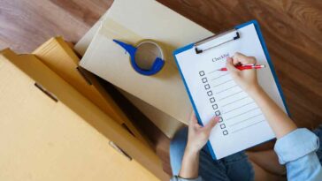Person checking off checklist of clip board leaning on top of moving boxes