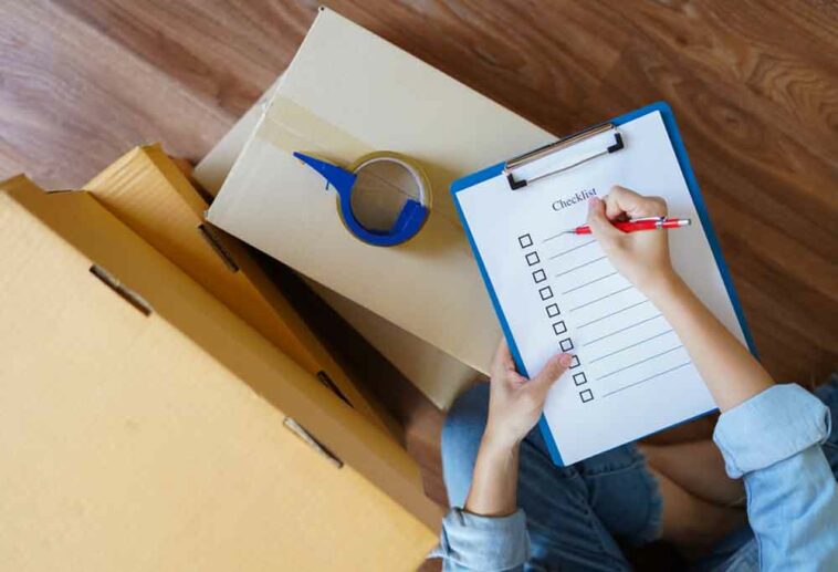 Person checking off checklist of clip board leaning on top of moving boxes